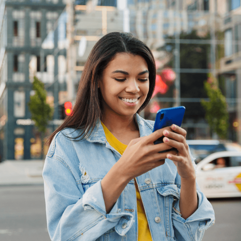 Career-Coaching-For-Employee-Engagement A young professional woman outside, using her phone to access Career Navigator. She is smiling, and confident in her new career coaching programme.