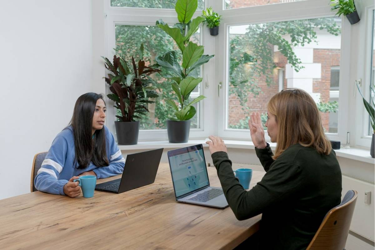 2 women sat opposite each other with laptops in front of them speaking